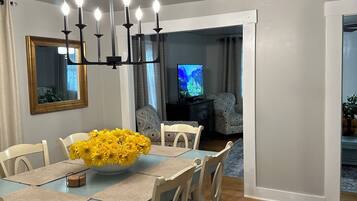 A dining area with a table set for four, a chandelier, and a television in the background.