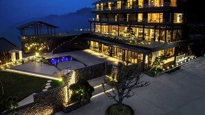 A multi-story hotel with a pool, outdoor lighting, and a view of the mountains. - In Cloud Resort Hotel (Yongzhou)