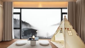A cozy room with a large window, a table with a lamp, a white cushion, and a teepee. - In Cloud Resort Hotel (Yongzhou)