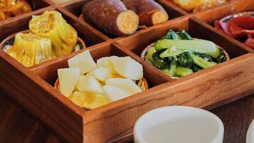 A wooden tray with various food items including corn, sweet potatoes, and greens.
