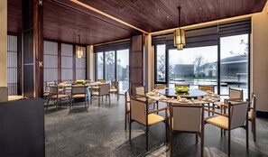 Een moderne eetruimte met ronde tafels en stoelen, grote ramen en een houten plafond.