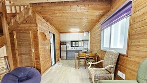 A cozy cabin interior with a wooden interior, a dining area with a table and chairs, and a kitchen in the background. - Tree Story Pension (Seogwipo)