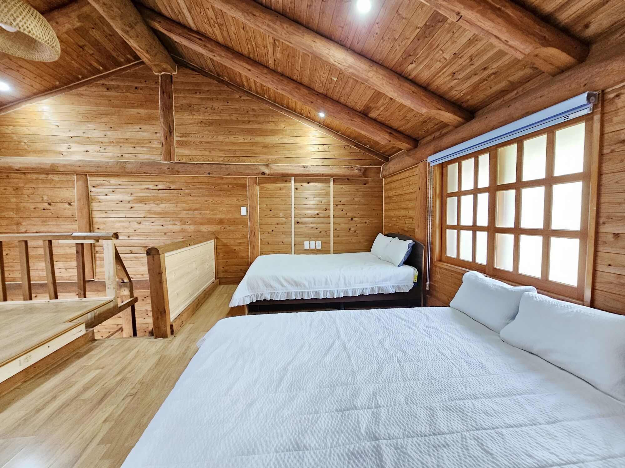Quarto de cabana de madeira com duas camas, uma escrivaninha e uma janela grande.