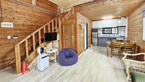 A cozy cabin interior with a wooden staircase, a kitchen area, and a seating area with a bean bag and chairs. - Tree Story Pension (Seogwipo)