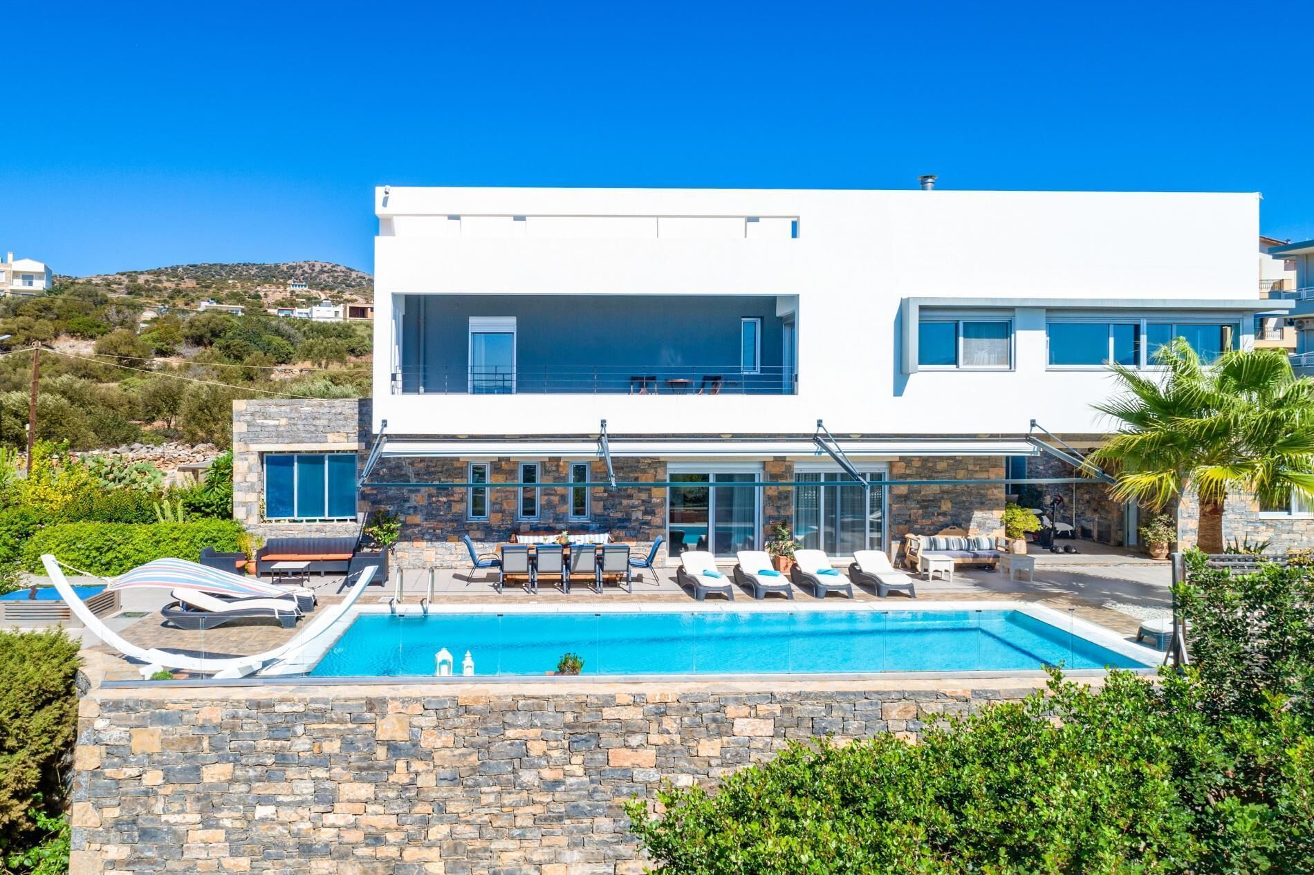 Una casa moderna de dos pisos con piscina, mobiliario exterior y fachada de piedra.
