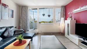 Ein modernes Wohnzimmer mit einem schwarzen Ledersofa, einem Couchtisch mit Pflanze, einem Fernseher und einem großen Fenster mit Blick auf die Stadt.