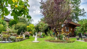 Un jardin avec une maison en bois, diverses plantes et une statue.