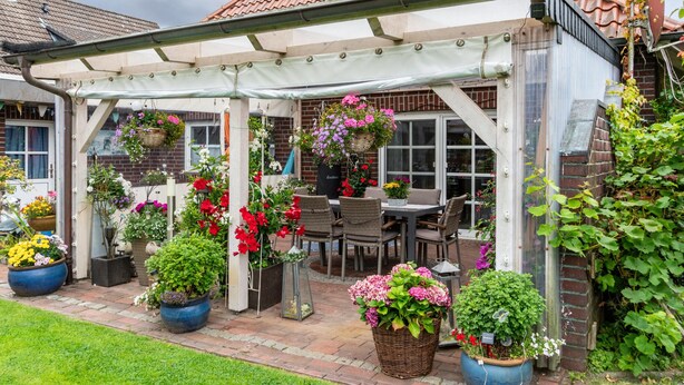 Un patio couvert avec une table et des chaises, entour é de plantes en pot et de suspensions florales.
