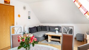 Un salon moderne avec un canapé d’angle gris, une table basse en bois et un petit pouf gris.
