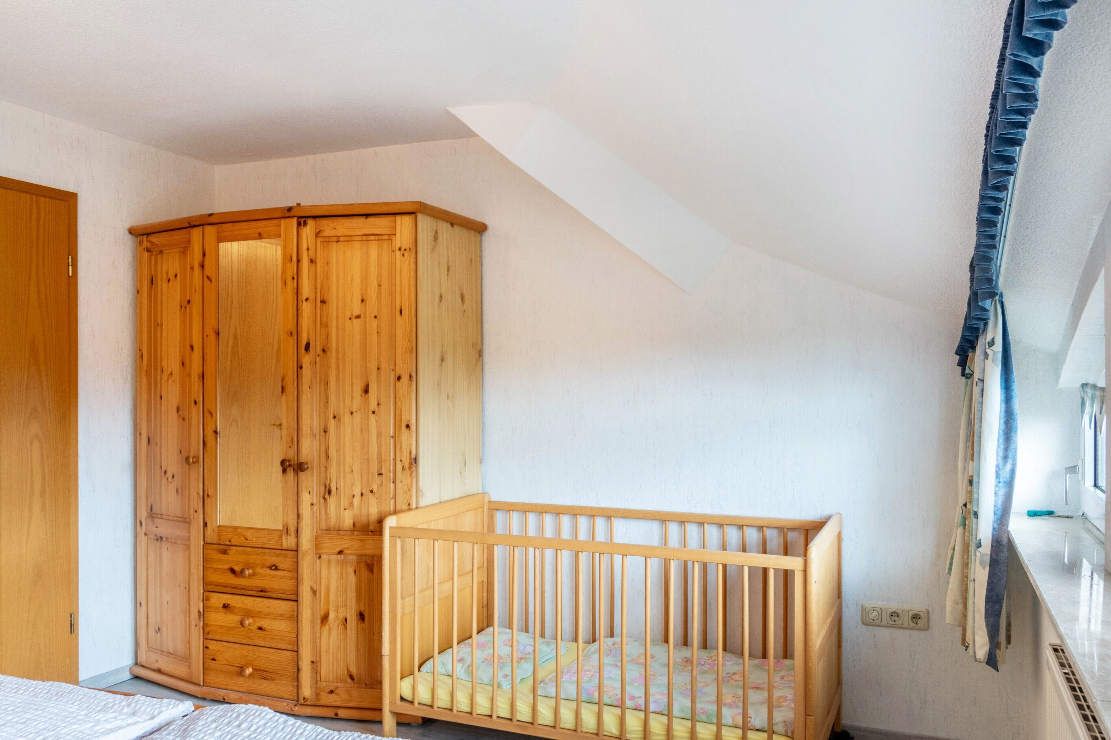 Een kamer met een houten garderobe, een houten wieg en een schuine balkenkap.