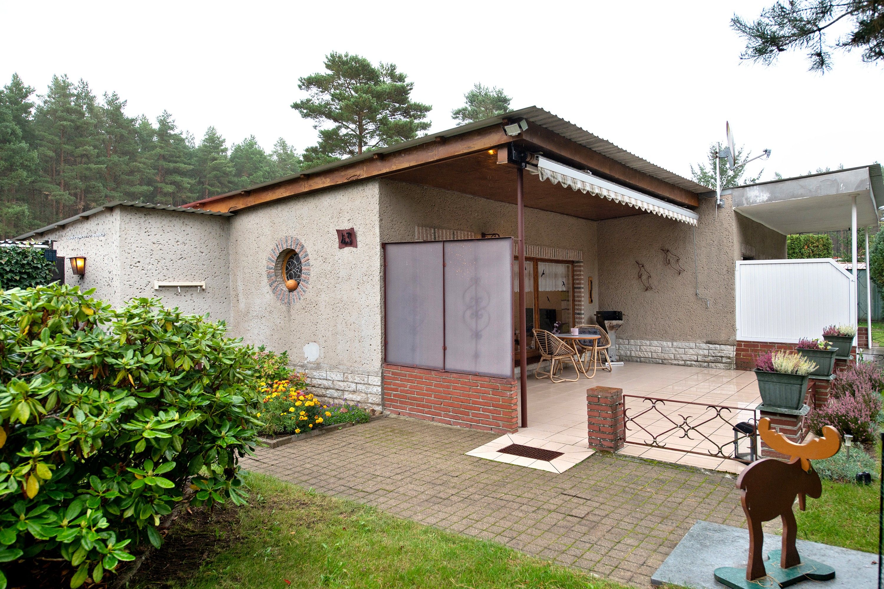 Un bâtiment de style rustique, avec une façade en briques, un patio couvert agrémenté de mobilier d’extérieur et, au premier plan, une sculpture décorative représentant un taureau.