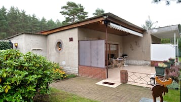 Un bâtiment de style rustique, avec une façade en briques, un patio couvert agrémenté de mobilier d’extérieur et, au premier plan, une sculpture décorative représentant un taureau.
