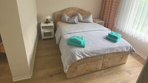 Ein Schlafzimmer mit einem hölzernen Bett, einem Nachttisch, einer Wandleuchte und einem Fenster mit Vorhängen.