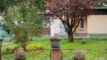 Un jardin avec un mur de briques, une clôture en métal et un arbre aux feuilles rouges.