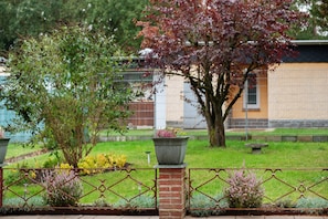 Un jardín con un muro de ladrillo, una valla metálica y un árbol de hojas rojas.