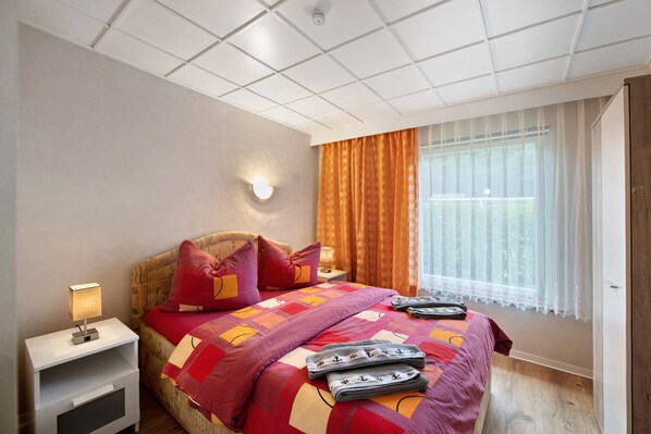 A hotel room with a bed, a nightstand, a lamp, a window with curtains, and a ceiling with recessed lighting.