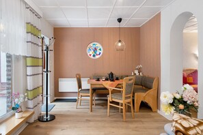 A cozy dining area with a wooden table, chairs, and a bench. There is a radiator, a floor lamp, and a wall-mounted light fixture.