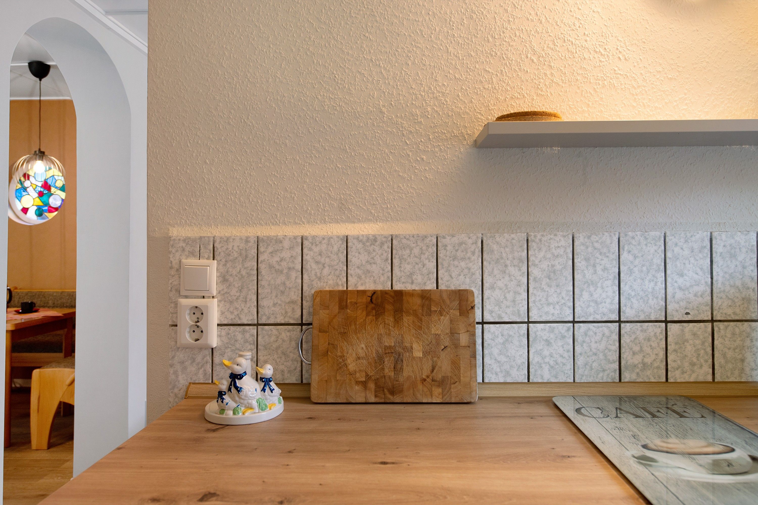 A kitchen with a wooden countertop, a cutting board, a wall-mounted light fixture, and a small decorative duck figurine.