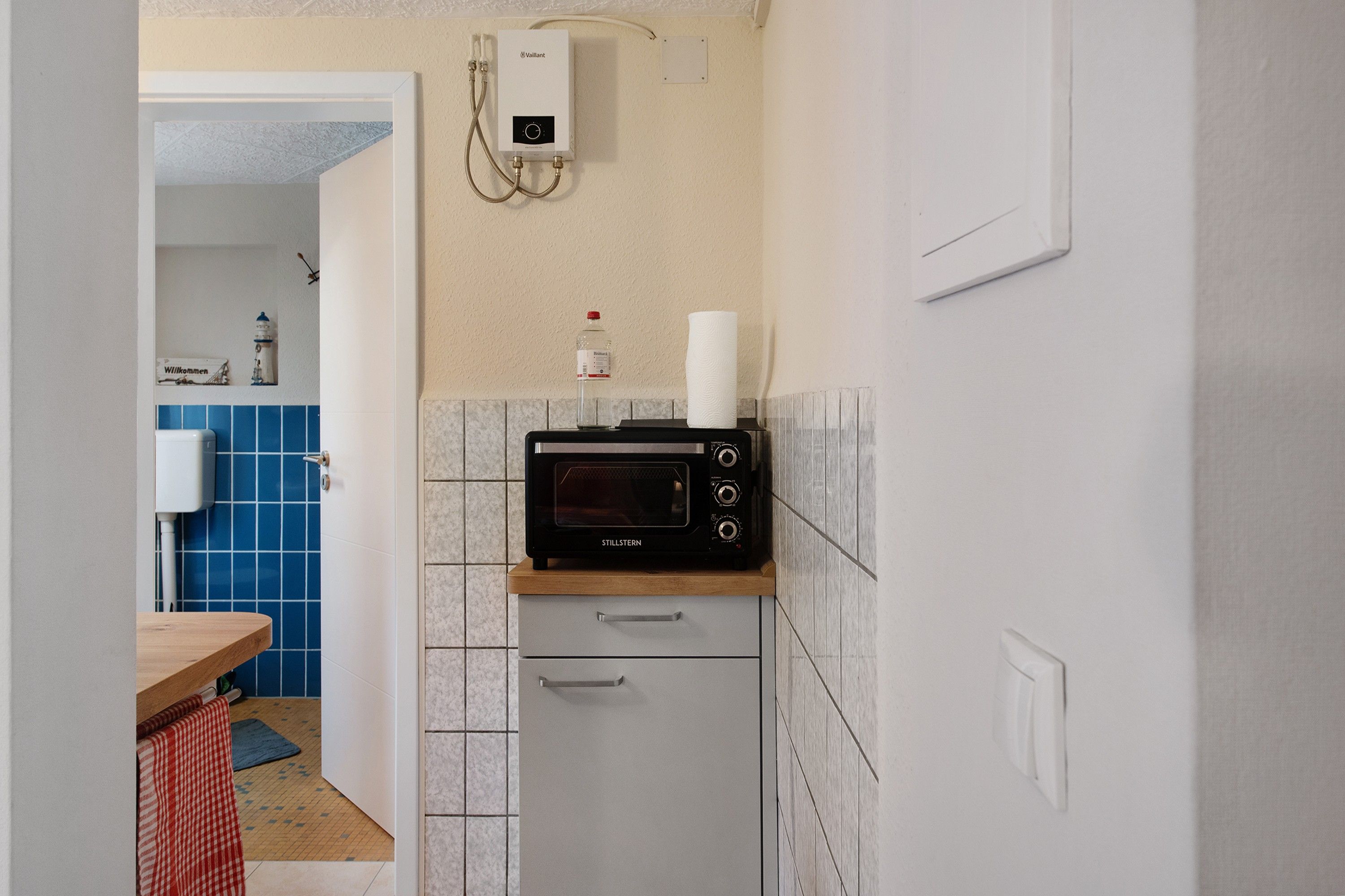Eine kompakte Küchenzeile mit einer Mikrowelle auf einer Holz Arbeitsplatte, einem kleinen Backofen darunter und einem an der Wand montierten Wasserhahn.
