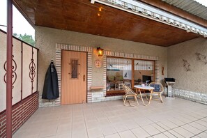 A covered patio area with a wooden door, a glass window, a wall-mounted lantern, and outdoor furniture.