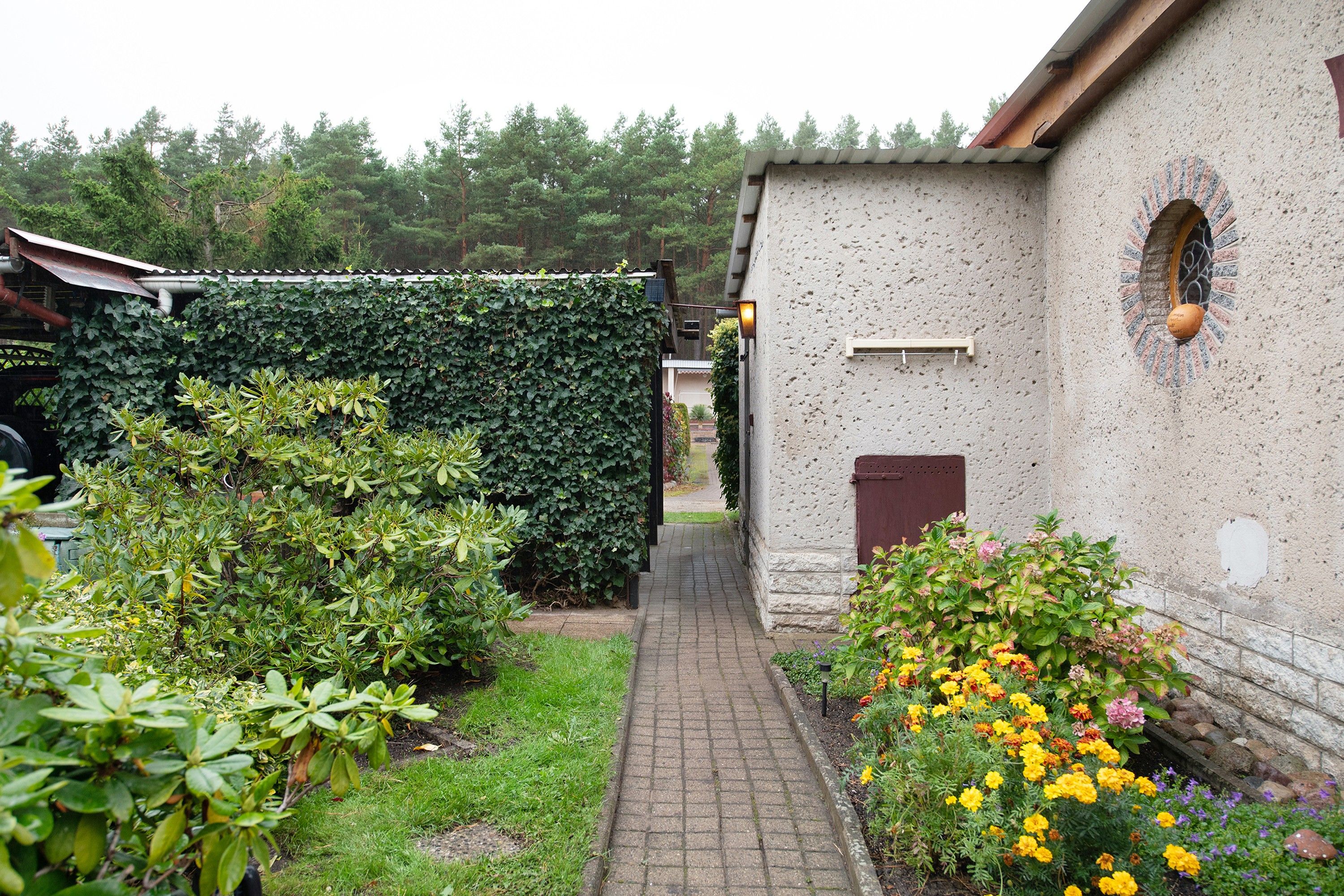A narrow paved pathway leading to a building with a textured wall and a small window.