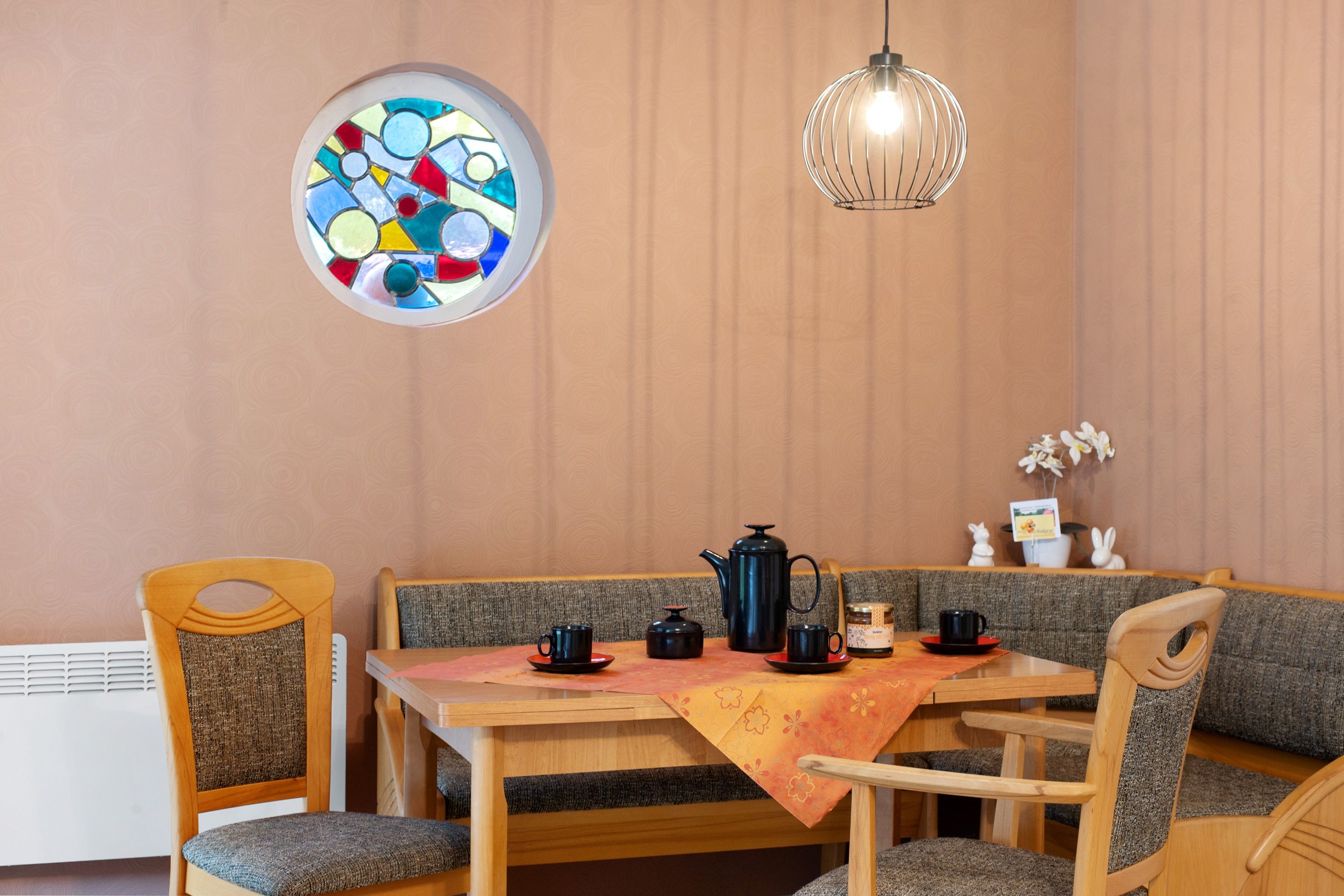 A dining area with a round table, chairs, a hanging light fixture, and a stained glass window.