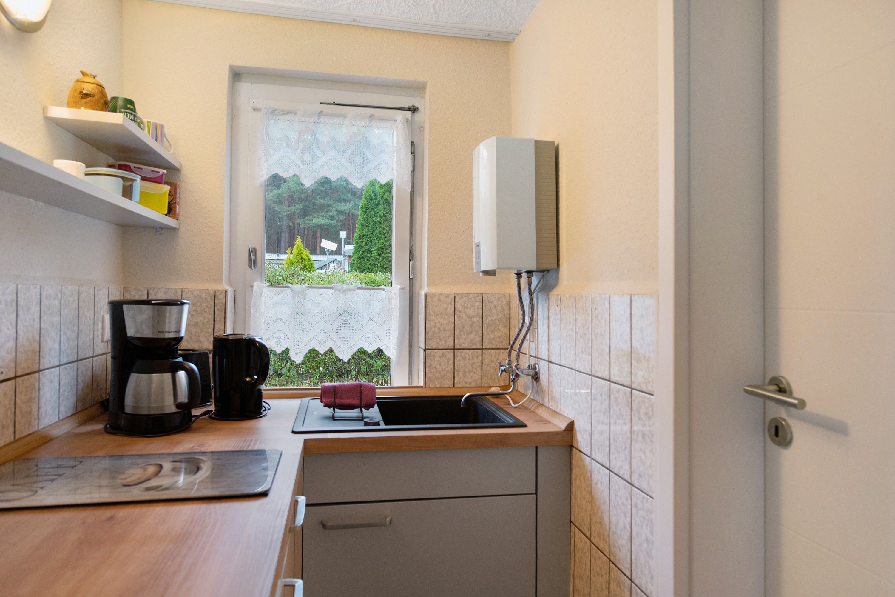 A compact kitchen with a coffee maker, a mug, and a towel on the counter. There's a window with a view of greenery outside.