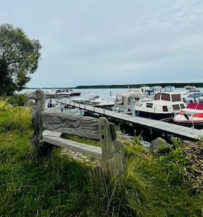 Un port de plaisance avec des bateaux amarrés, une jetée en bois et un grand arbre au premier plan.