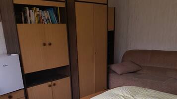 A bedroom with a bed, a wardrobe, and a small desk with a refrigerator.