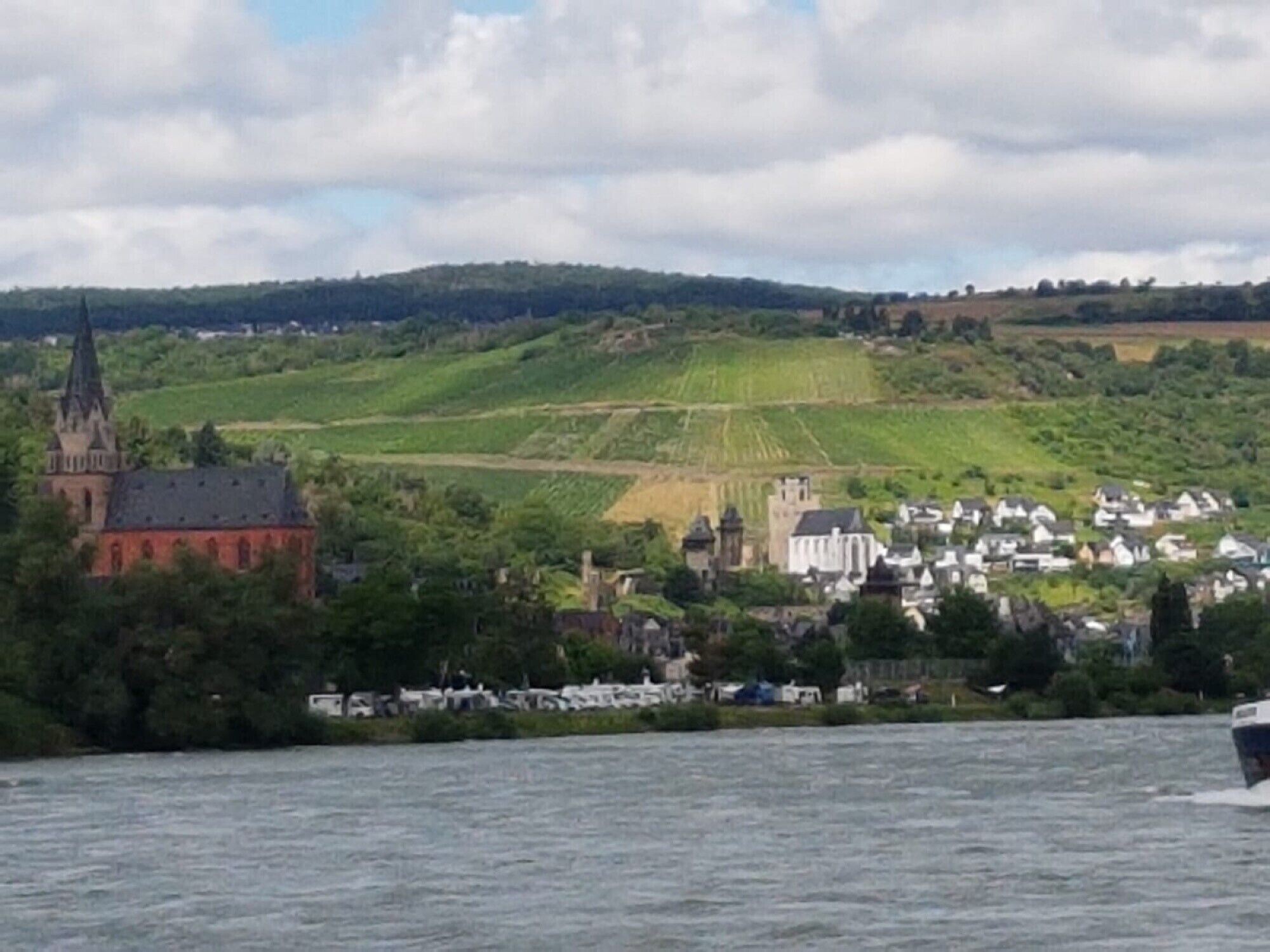 Ein Fluss mit einem Boot, einer Kirche und einer Stadt am gegenüberliegenden Ufer.