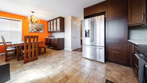A kitchen with wooden cabinets, a stainless steel refrigerator, and a dining area with a wooden table and chairs. - Celest Homes! Spacious, family home, right  for your next family adventure.  (Edmonton)