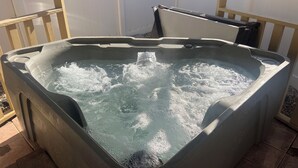 A hot tub with water, surrounded by a wooden deck and a white wall.