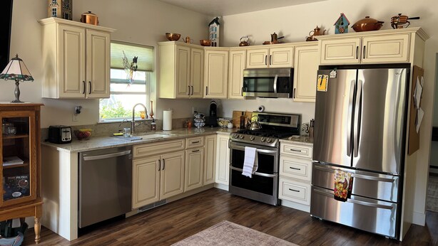 A modern kitchen with light-colored cabinets, stainless steel appliances, and a wooden floor.