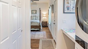 A hallway with wooden flooring, white doors, a bed, a nightstand, and a framed picture on the wall.
