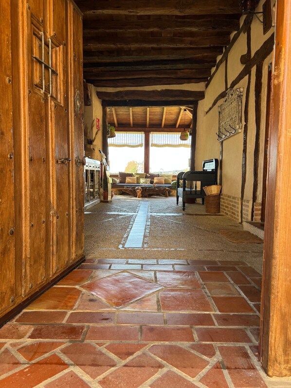 Un interior rústico con una puerta de madera, suelo de piedra, un banco y vistas por una ventana.