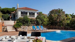 A poolside dining area with a table set for four, a pool, and a house with a balcony.
