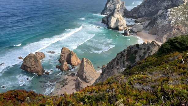 A coastal landscape with rocky formations and a beach.