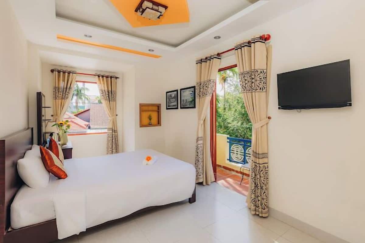 A hotel room with a bed, a TV mounted on the wall, and a window with curtains.
