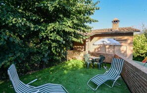 A backyard with a brick wall, a table with chairs, and two striped lounge chairs.