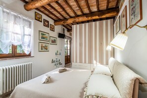 A bedroom with a wooden ceiling, a bed with white bedding, a radiator, and striped wallpaper.