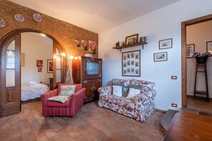 A room with a brick archway, a wooden door, a television, a floral sofa, a red armchair, and a wooden table.