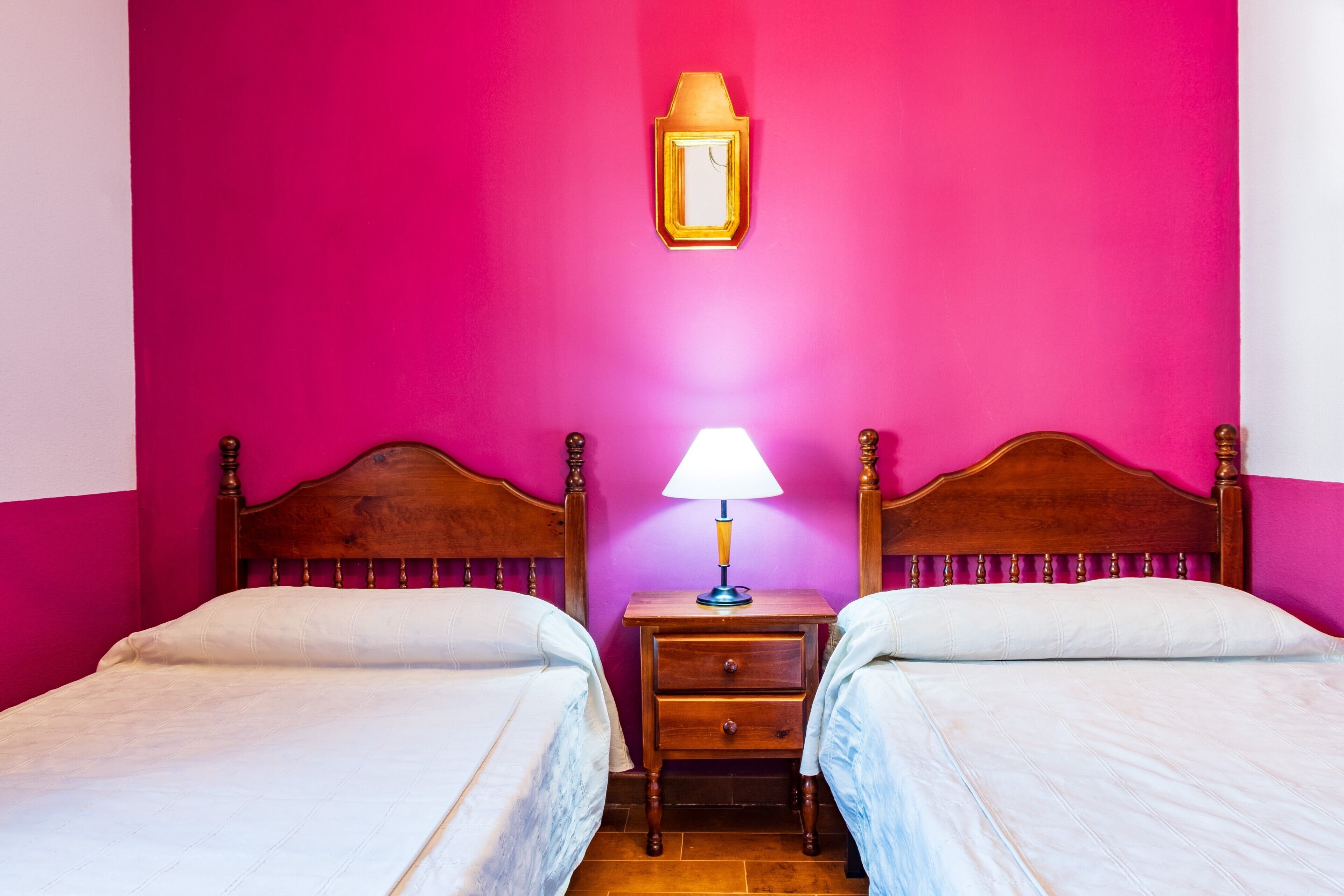 A room with two beds, a nightstand with a lamp, and a wall-mounted light fixture.