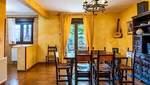 Un comedor con mesa y sillas de madera, una araña y una guitarra en la pared.