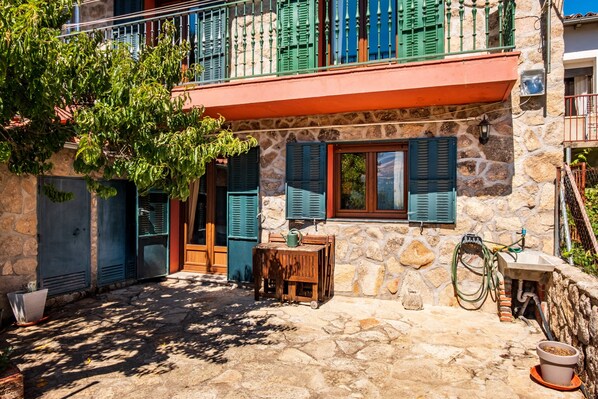 A stone building with a balcony, a wooden table, and a potted plant.