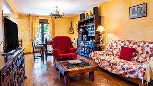 Una sala de estar acogedora con un sofá, un sillón rojo, una mesa de centro de madera, una guitarra y una estantería.