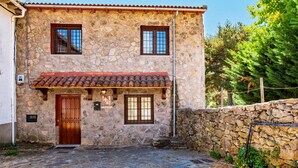 Un edificio de piedra con techo de tejas rojas, una puerta de madera y dos ventanas con marcos marrones.