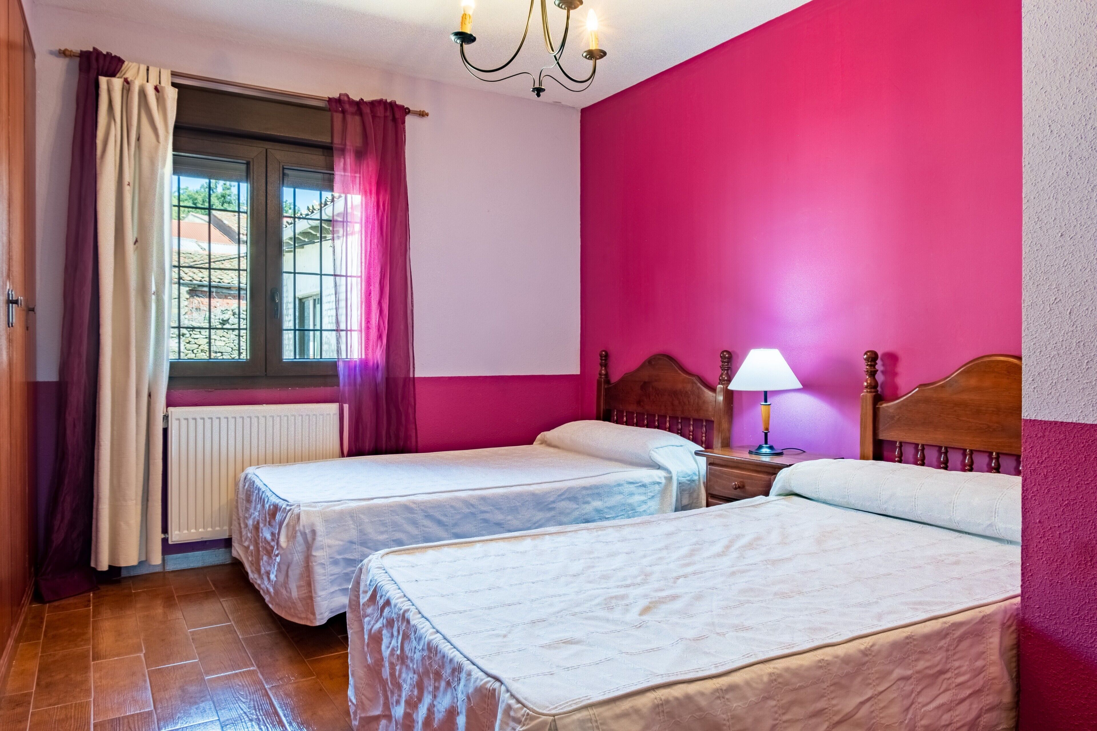 Une chambre avec deux lits, une fenêtre avec des rideaux, un radiateur et un lustre.