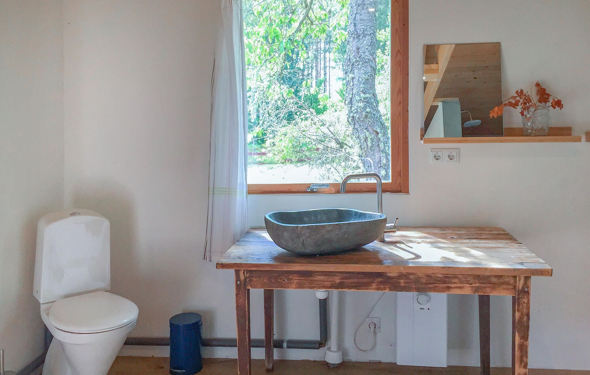 A bathroom with a white toilet, a wooden sink table, and a window with a view of trees.