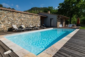 Una piscina con sillas de descanso, un muro de piedra y una terraza de madera.