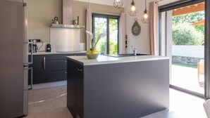 A modern kitchen with a central island, stainless steel appliances, and a view of the outdoors. - Holiday Home 'Villabergerie En Pierre Du Pays' with Private Pool, Wi-Fi and Air Conditioning (Barbaggio)